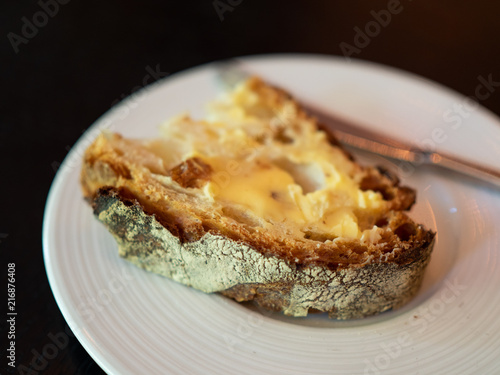 A slice of freshly baked bread with good quality French butter on a white plate. Simple yet tasty and delicious. Natural light. Selective Focus.