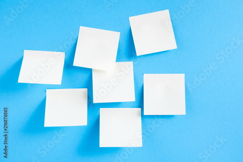 Blank white sticky notes on blue background, concept of business work. White memo stickers on blue wall. Mock-up 