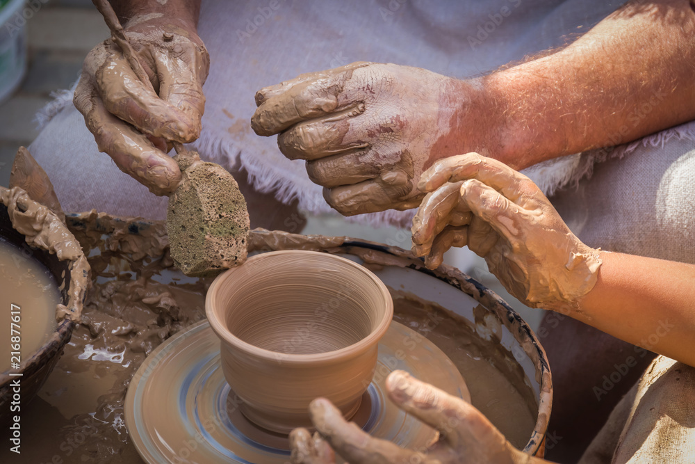 The hands of the potter's master show the secrets of making clay products and direct the children's hands in making a jug of clay