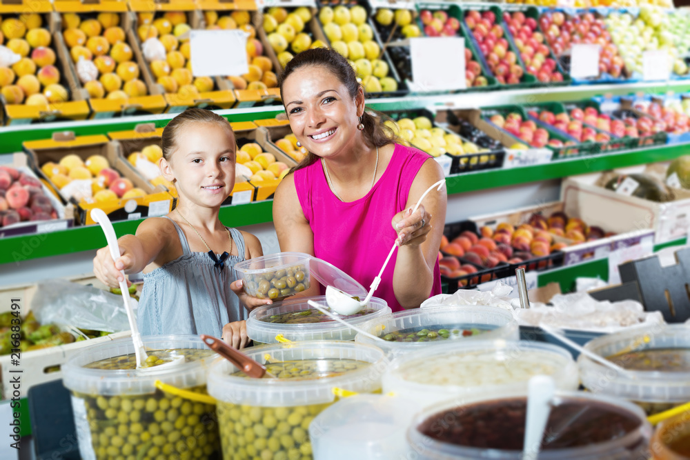 Happy mother with girl taking tasty olives to container