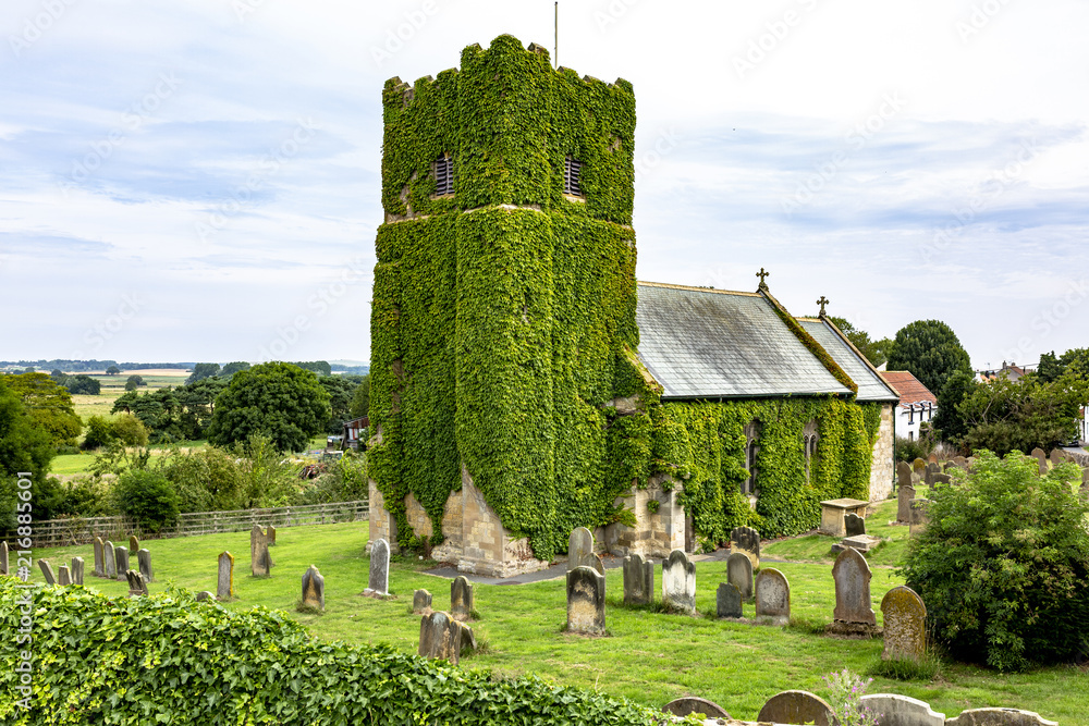 Old Church bell tower overgrown with lush green ivy, North Yorkshire, England.