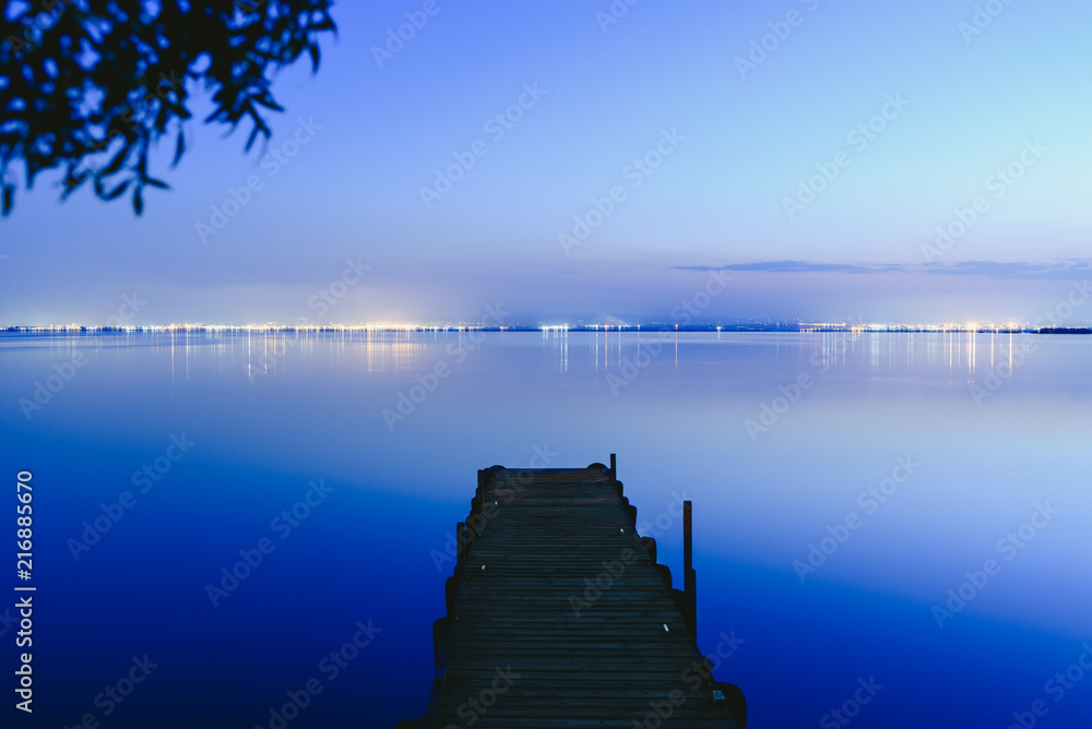 Pier on a lake at sunset with calm water and reflections of relaxing lights.