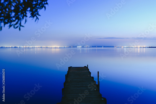 Fototapeta Naklejka Na Ścianę i Meble -  Pier on a lake at sunset with calm water and reflections of relaxing lights.