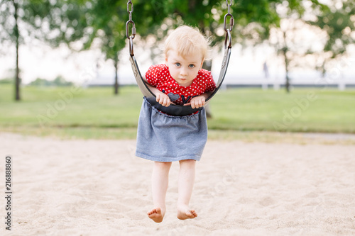 Portrait of happy smiling little toddler girl swinging on swings at playground outside on summer day. Happy childhood lifestyle concept. Toned with film pastel faded filters colors. © anoushkatoronto