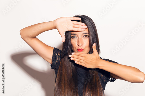Young adult woman framing her face with her hands, making funny faces. In studio over a white background.
