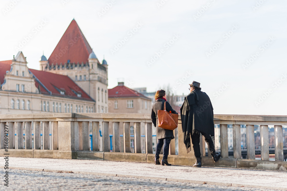 Couple standing on the bridge beside the ornate railing of the Spree riverbank at dusk. Waters of the river, canal in the background.