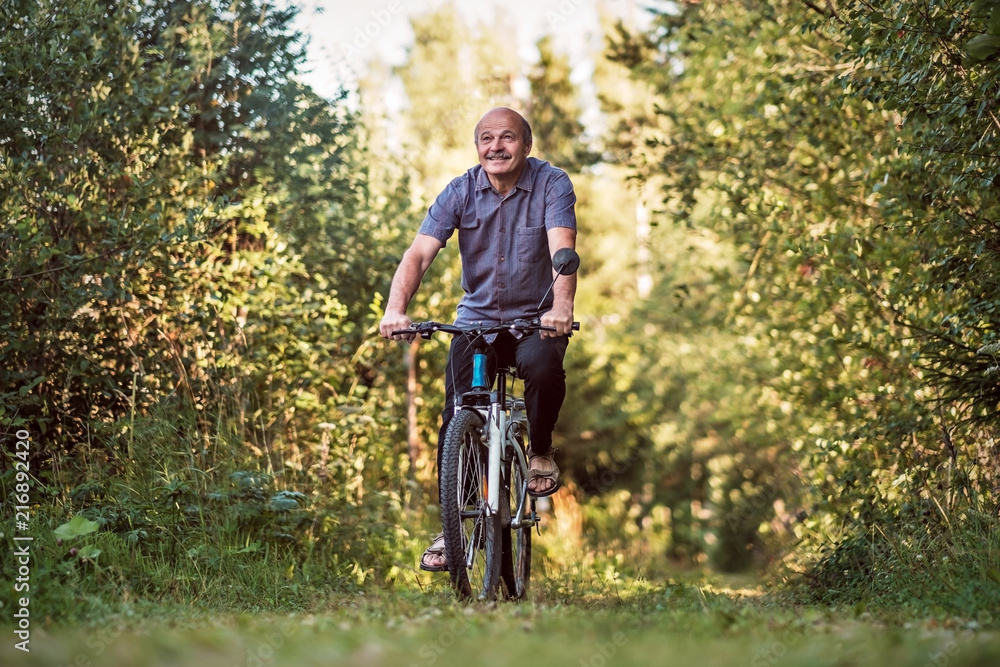 Joyful senior man riding a bike in a park on a beautiful sunny day