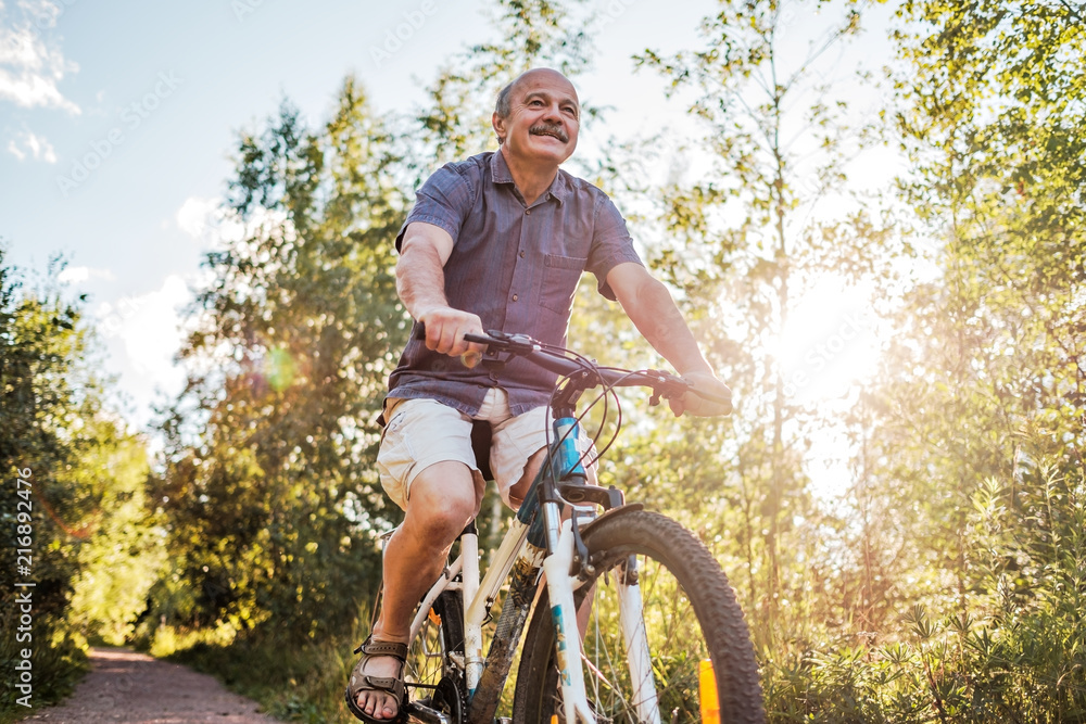 Fototapeta premium Joyful senior man riding a bike in a park on a beautiful sunny day