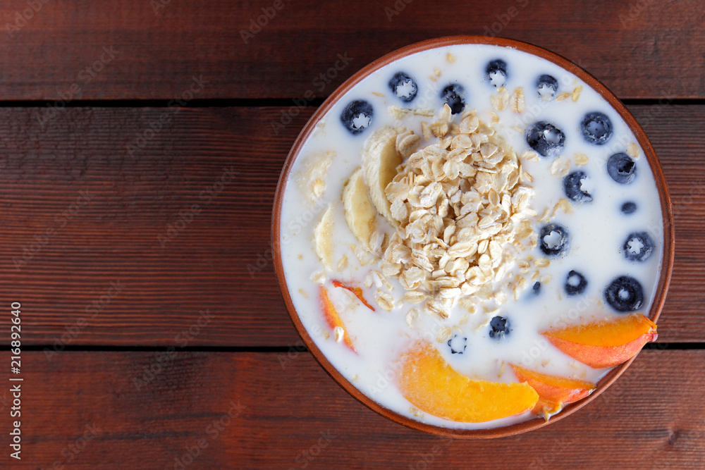 Oatmeal porridge with milk and fruit on a wooden background, healthy porridge with pieces of banana and peach, breakfast with fiber, calcium and vitamins, food for the schoolboy Oatmeal porridge with milk and fruit on a wooden background, healthy porridge with pieces of banana and peach, breakfast with fiber, calcium and vitamins, food for the schoolboy