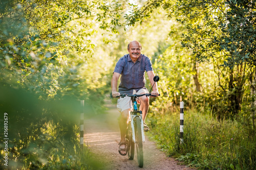 Joyful senior man riding a bike in a park on a beautiful sunny day