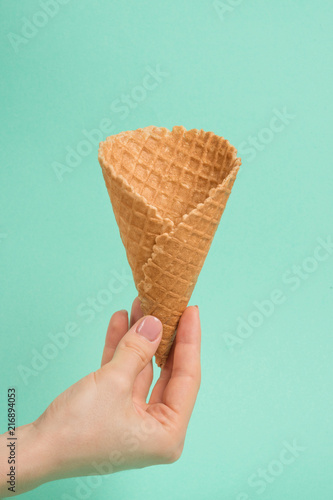 Female hand with waffle cone on mint background