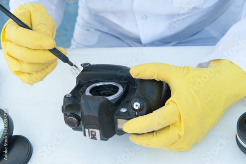 Elderly solid person in white dressing gown, cap, medical mask, glasses cleans matrix of digital camera with special means. Lens, sensor, matrix, cleaning wands, magnifier, isopropyl alcohol.