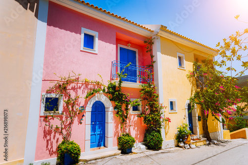 Assos village. Traditional colored greek houses with bright blue doors and windows. Blooming fucsia plant flowers growing around entrance welcome gates. Kefalonia island, Greece