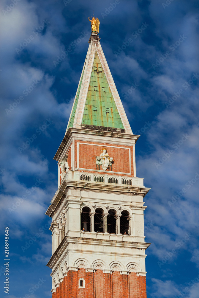 Saint Mark bell tower in the center of Venice with golden angel statue at the top and beautiful clouds