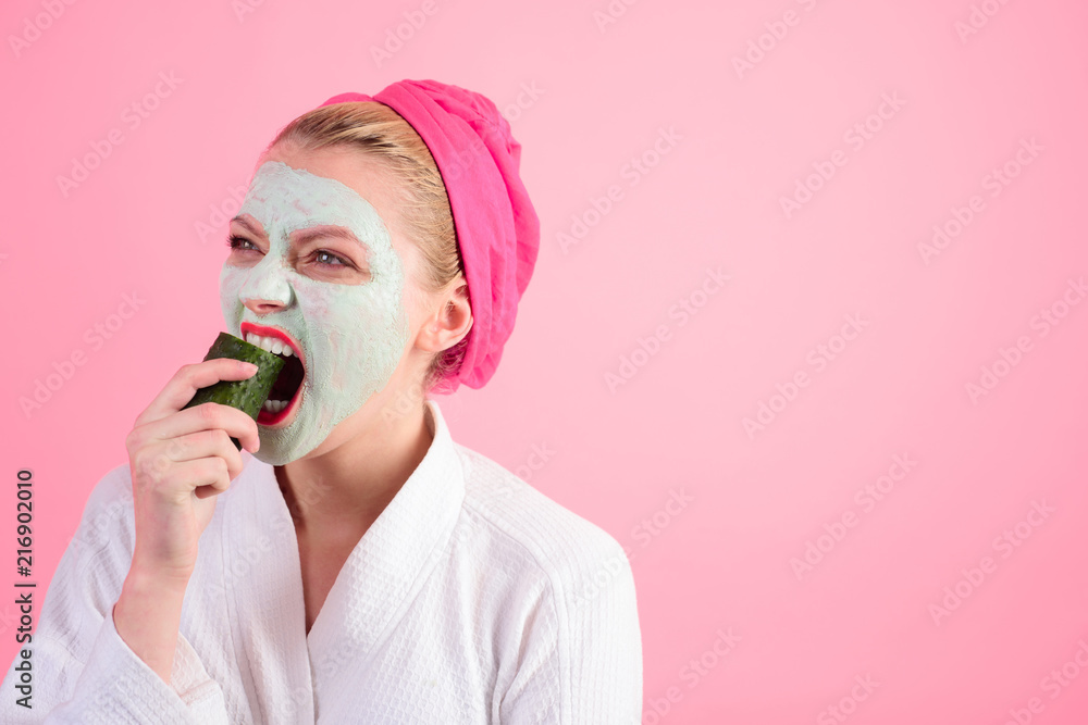 Cosmetic procedures. Woman with cosmetic mask on face eats cucumber