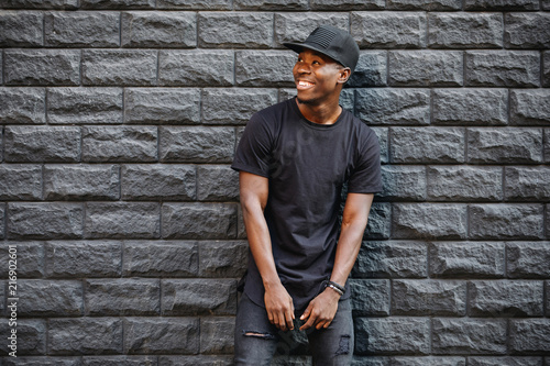 Handsome african american man in blank black t-shirt standing against brick wall