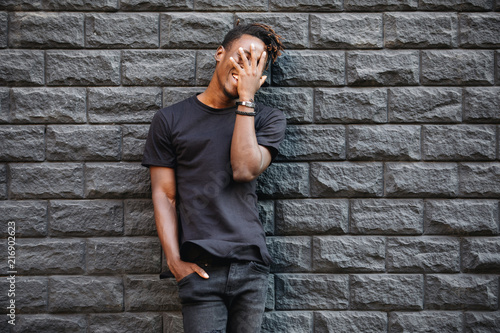 African american man in black t-shirt laughing against brick wall, palm on face