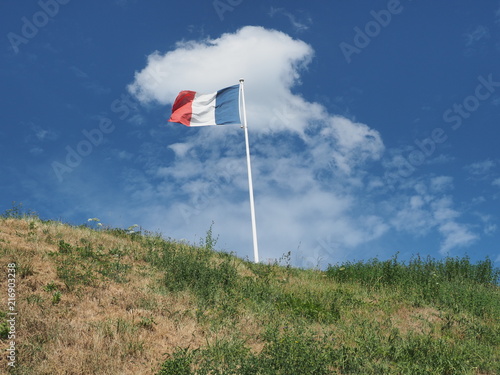 Nationalflagge von Frankreich vor blauem Himmel mit weißen Wolken auf grünem Hügel 