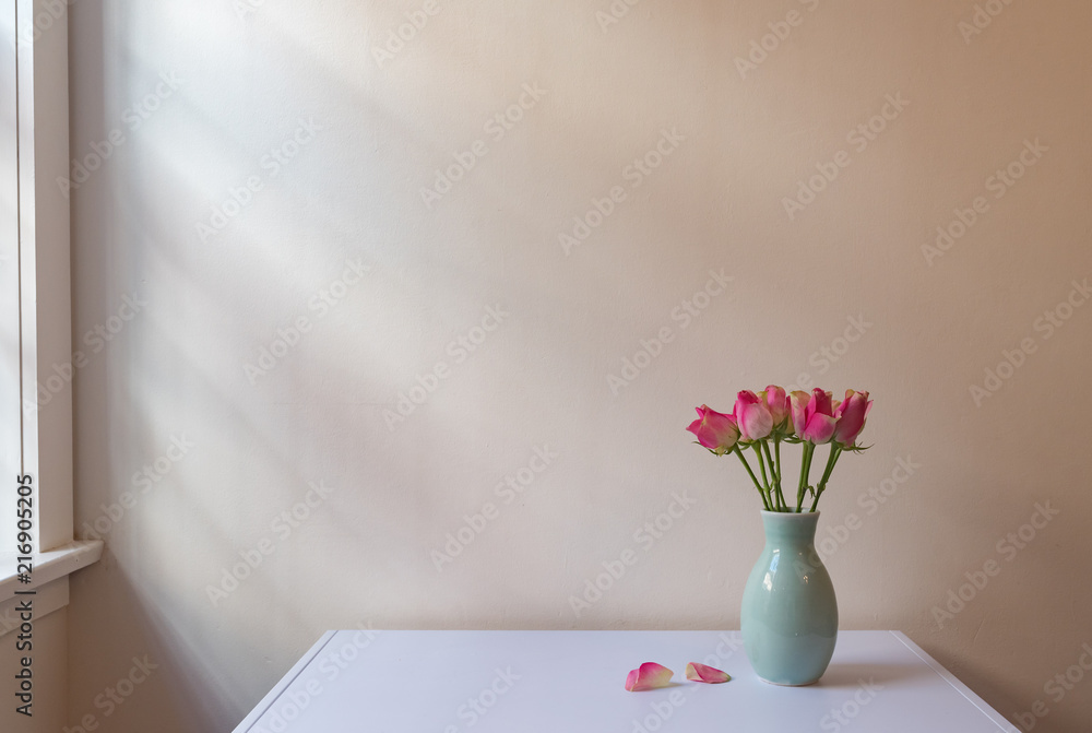 Obraz premium Pink roses in green vase on white table next to window with soft light and copy space (selective focus)