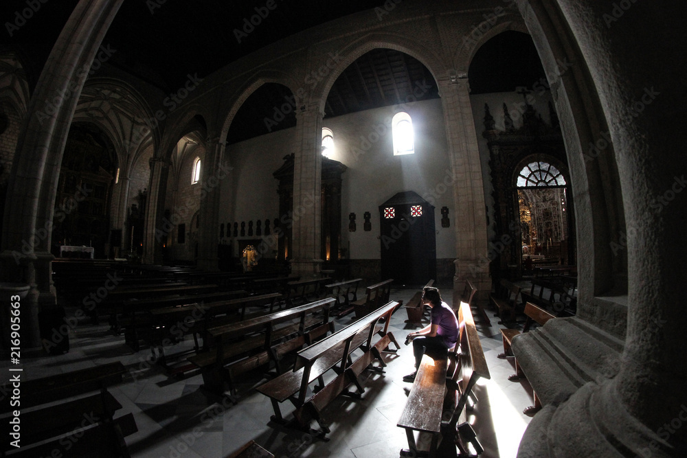 Obraz premium young man sitting alone inside a church in the light of a ray of sunlight coming through the window