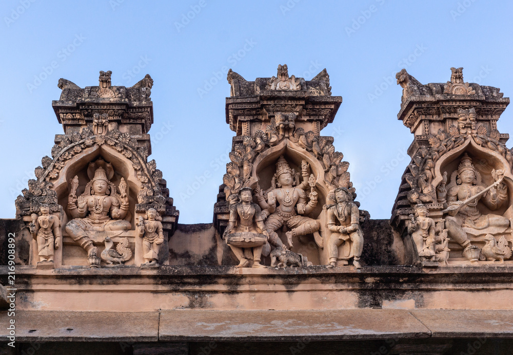 Shravanabelagola, Karnataka, India - November 1, 2013: Brown stone with black mold deity statues in niches on edge of roof at Jain Tirth building. Shiva, Vishnu and Saraswati.