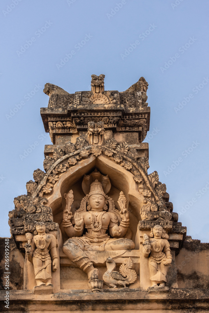 Shravanabelagola, Karnataka, India - November 1, 2013: Brown stone with black mold deity statue in niches on edge of roof at Jain Tirth building. Vishnu with two female deities.