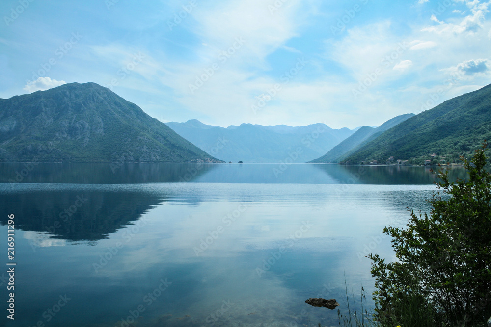 Bay of Kotor, also known as Kotorska Boka, during a quiet summer afternoon with mountains reflecting in the waters of the Adriatic sea. The gulf of Kotor is one of most iconic landmarks of Montenegro.