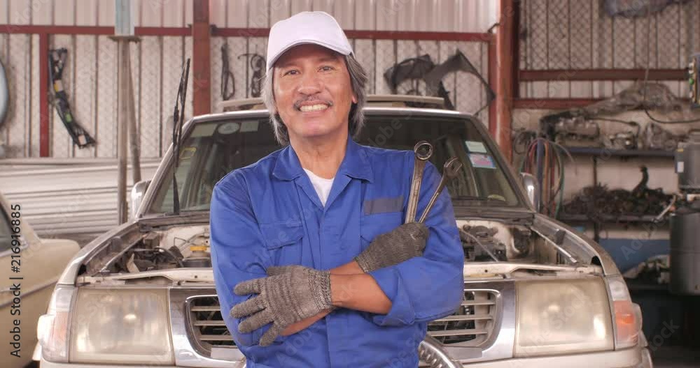Portrait of professional mechanic in a car workshop, repair station, standing with arms crossed, spanner in hands, car service concept. Portrait of professional mechanic in a car workshop, repair station, standing with arms crossed, spanner in hands, car service concept.