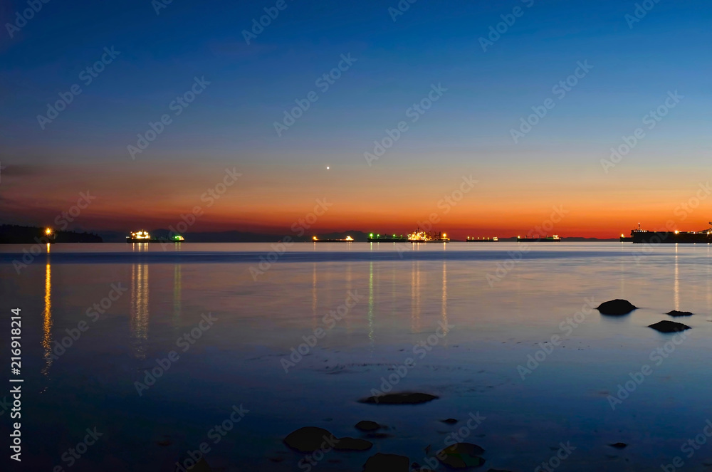 Cargo ships in harbor near Vancouver at night. Long treks of ship lights in the dark water. Colourful image. Vancouver. British Columbia. Canada.
