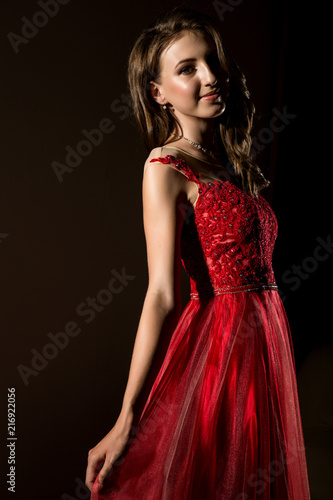 Sensual beautiful young woman posing in red dress in dark room. professional make-up