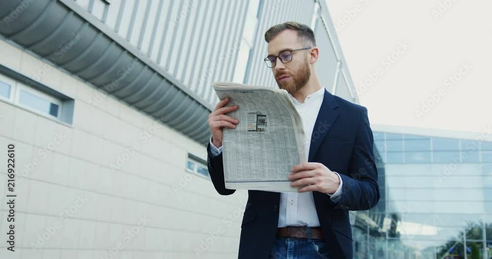 Caucasianoffice worker walking to the work in the morning and reading newspaper while stepping. Outdoors.