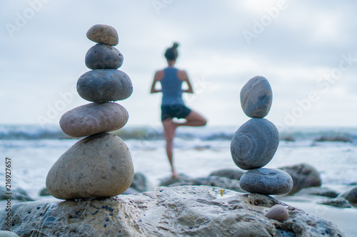 Фотография Beautiful girl tree pose yoga by the ocean with stacking rocks