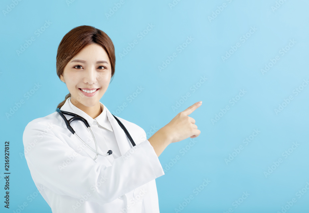 Smiling female doctor pointing with finger on blue background Smiling female doctor pointing with finger on blue background