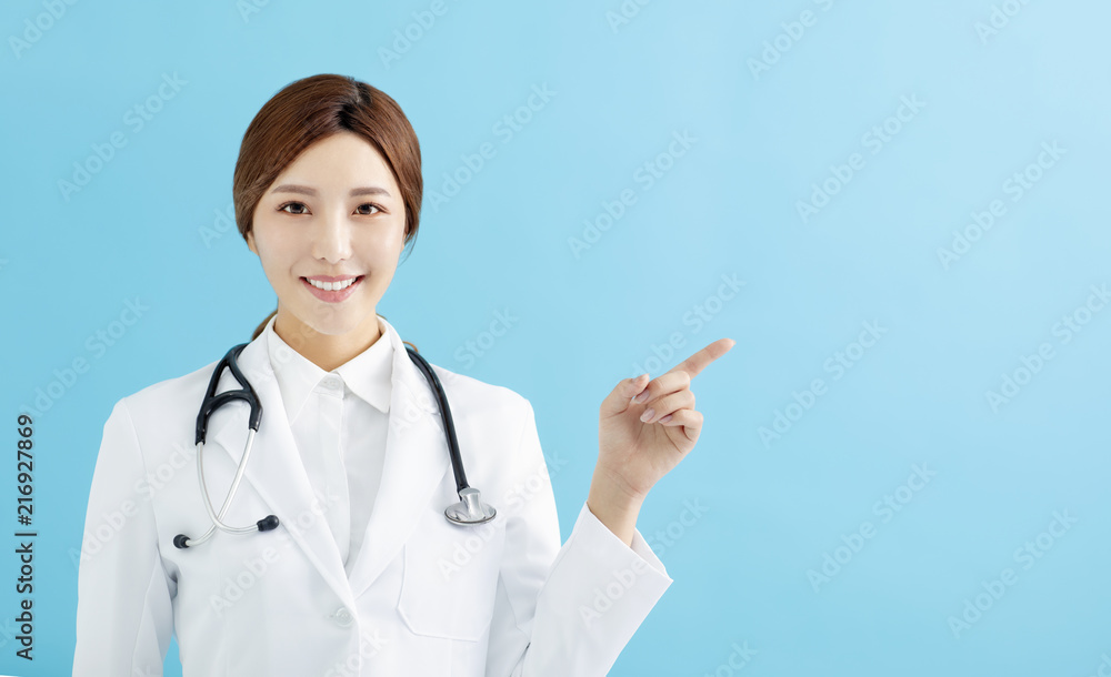 Smiling female doctor pointing with finger on blue background Smiling female doctor pointing with finger on blue background