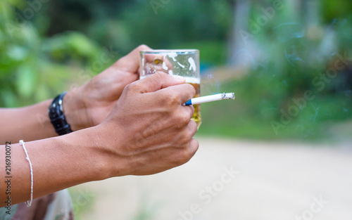 Hand with burning cigarette and hands holding up glasses of beer