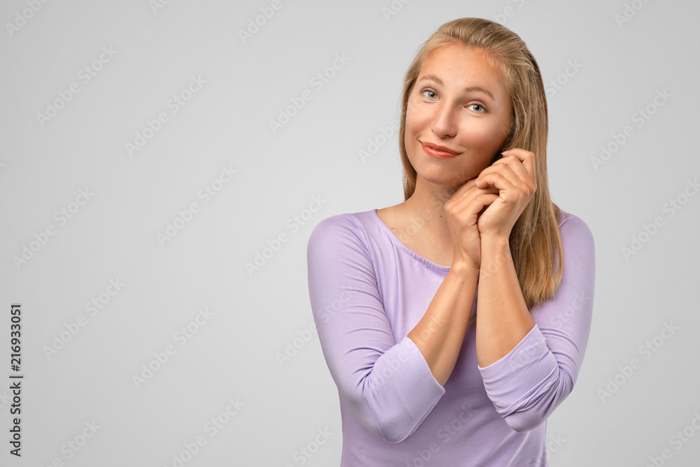 He is my hero. Portrait of beautiful blonde european woman in love, holding clasped hands over chest, looking aside in shy and tender pose, smiling, dreaming about something lovely over gray wall He is my hero. Portrait of beautiful blonde european woman in love, holding clasped hands over chest, looking aside in shy and tender pose, smiling, dreaming about something lovely over gray wall