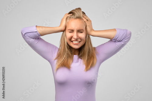 Mad crazy young woman in blue t shirt with hands on head and eyes closed standing and suffering from headache isolated over white background