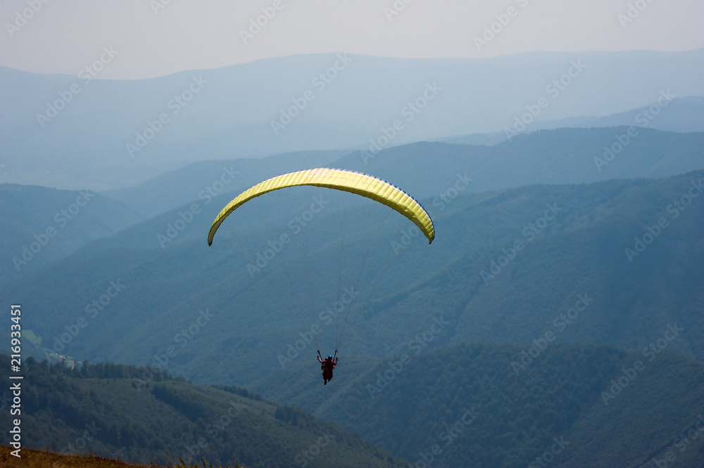 Paraglider flies over a mountain valley on a sunny summer day. Paragliding in the Carpathians in the summer. Paraglider flies over a mountain valley on a sunny summer day. Paragliding in the Carpathians in the summer.