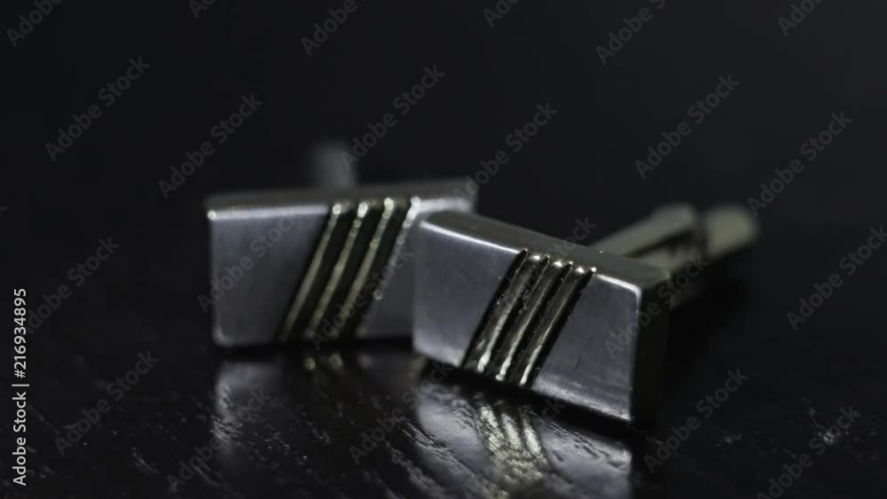 Silver cufflinks lie on a black table close-up, backlit Silver cufflinks lie on a black table close-up, backlit