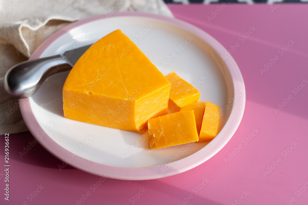Triangle piece of British hard cow dark yellow cheddar cheese on pink table Triangle piece of British hard cow dark yellow cheddar cheese on pink table