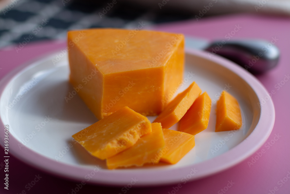 Triangle piece of British hard cow dark yellow cheddar cheese on pink table Triangle piece of British hard cow dark yellow cheddar cheese on pink table