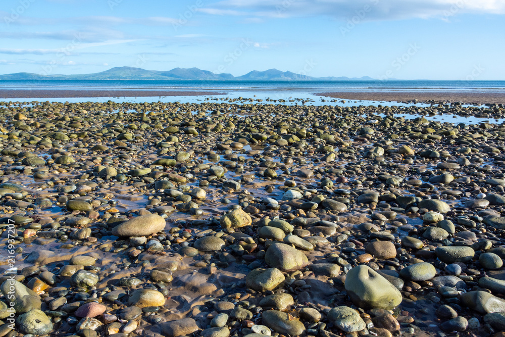 Pebbles on a beach of Anglesey and mountains of Snowdonia across the Menai Strait