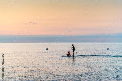 silhouette of father and son standing on Stand Up Paddle Board. SUP. in beatutiful sunset at the beach in a quiet scene. 