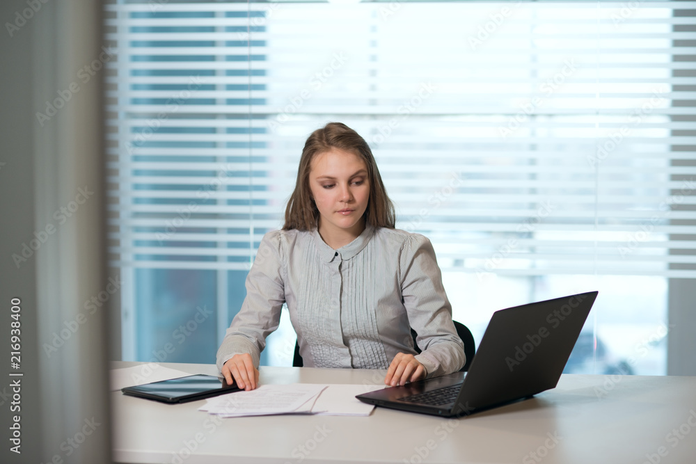 young girl businesswoman in casual clothes, sitting at a table closely look at documents, working at computer young girl businesswoman in casual clothes, sitting at a table closely look at documents, working at computer