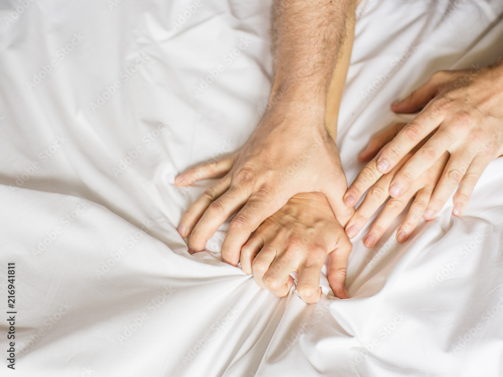 Couple having sex. Hand clutches grasps a white crumpled bed sheet in a hotel room, a sign of ecstasy, feeling of pleasure or orgasm Couple having sex. Hand clutches grasps a white crumpled bed sheet in a hotel room, a sign of ecstasy, feeling of pleasure or orgasm