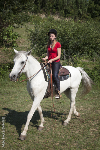 young teen girl in red shirt on white horse in green surroundings