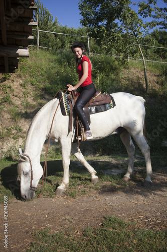 young teen girl in red shirt on white horse in green surroundings © ahavelaar