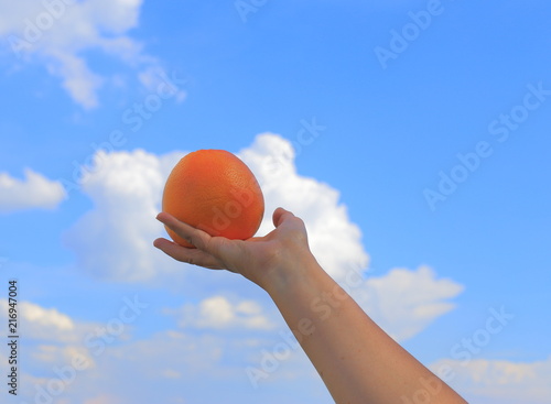 Beauty of nature, women and healthy eating. The woman's hands hold a grapefruit against the sky and clouds. A close-up photo.