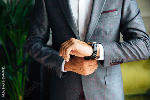 A close-up of a cropped frame of a stylish slender man in a jacket looks at his watch. Businessman is watching time  hurrying to an important meeting. Concept office  business  style  business suit.