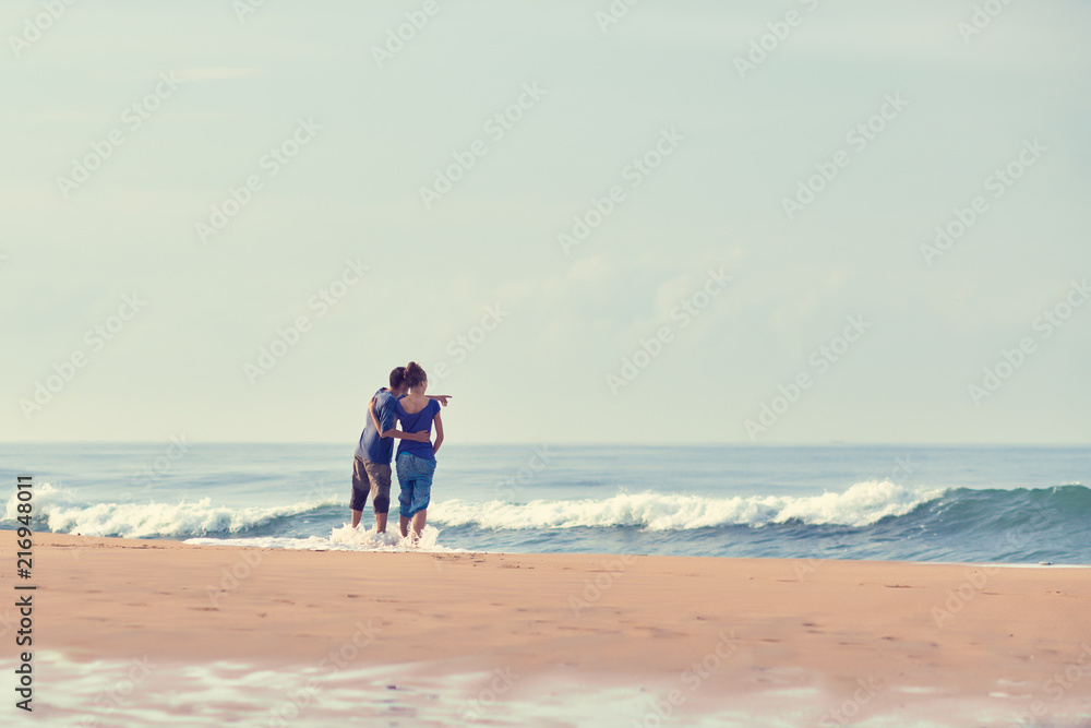 Young Couple standing on beach and looking to a sea. A man is showing his hand in the sea. Young Couple standing on beach and looking to a sea. A man is showing his hand in the sea.